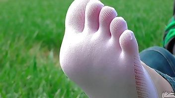 Goddess feet in cute white socks with jeans on the spring grass field